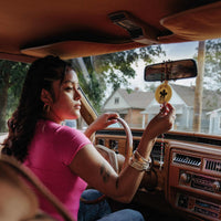Driver hanging a Buena Vibra car freshener from a rearview mirror