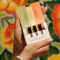 Hand holding Nopalera Fragrance Discovery Trio with three mini perfume sprays against a colorful floral background