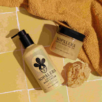 Nopalera body care products on a yellow tiled floor with a towel and sponge.