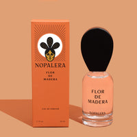 A glass of a 50ml Luxury Mexican fragrance bottle of Flor de Madera perfume with a wooden cap, alongside its orange packaging box with the brand name Nopalera and product title.