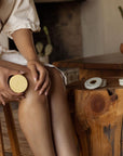 Person applying Nopalera citrus lotion bar to legs in a natural setting.