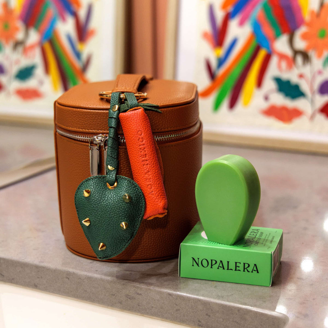 Nopalera cactus soap with green soap dish and leather keychain accessories displayed next to a brown leather travel case on a countertop.