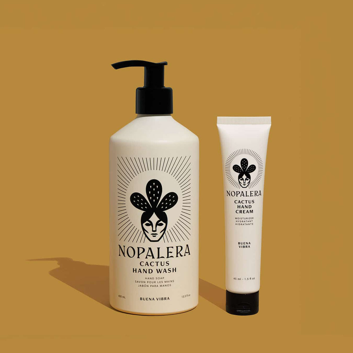Nopalera Cactus Hand Wash in a cream-colored pump bottle and Cactus Hand Cream tube in Buena Vibra scent, side by side on a mustard-yellow background.