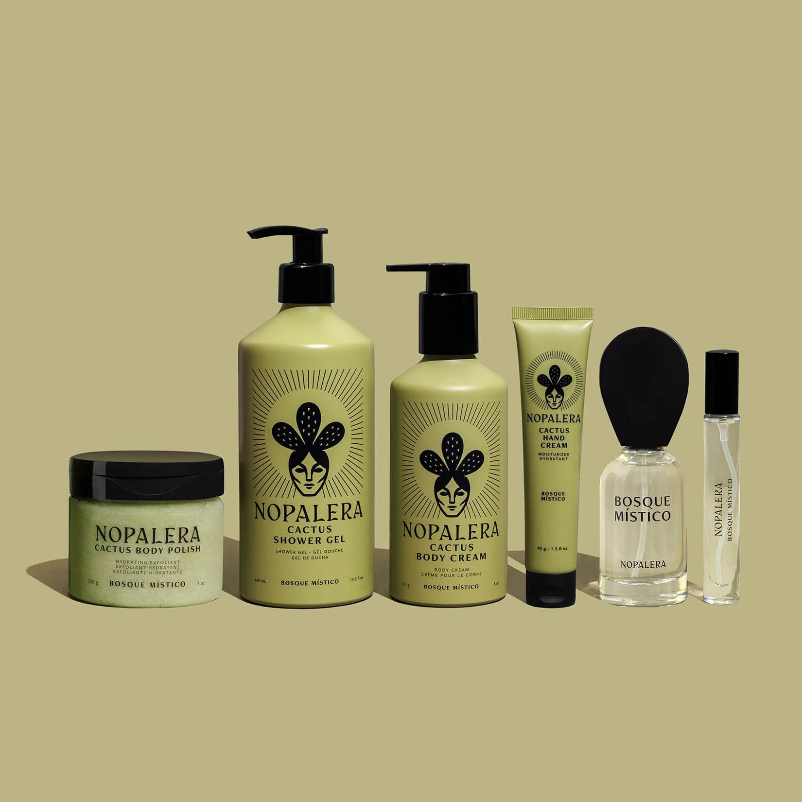 A set of Nopalera Bosque Místico skincare products arranged on a green background, including a cactus shower gel bottle, a body  polish, a body  cream, a hand cream, a 50 ml perfume and a travel spray.