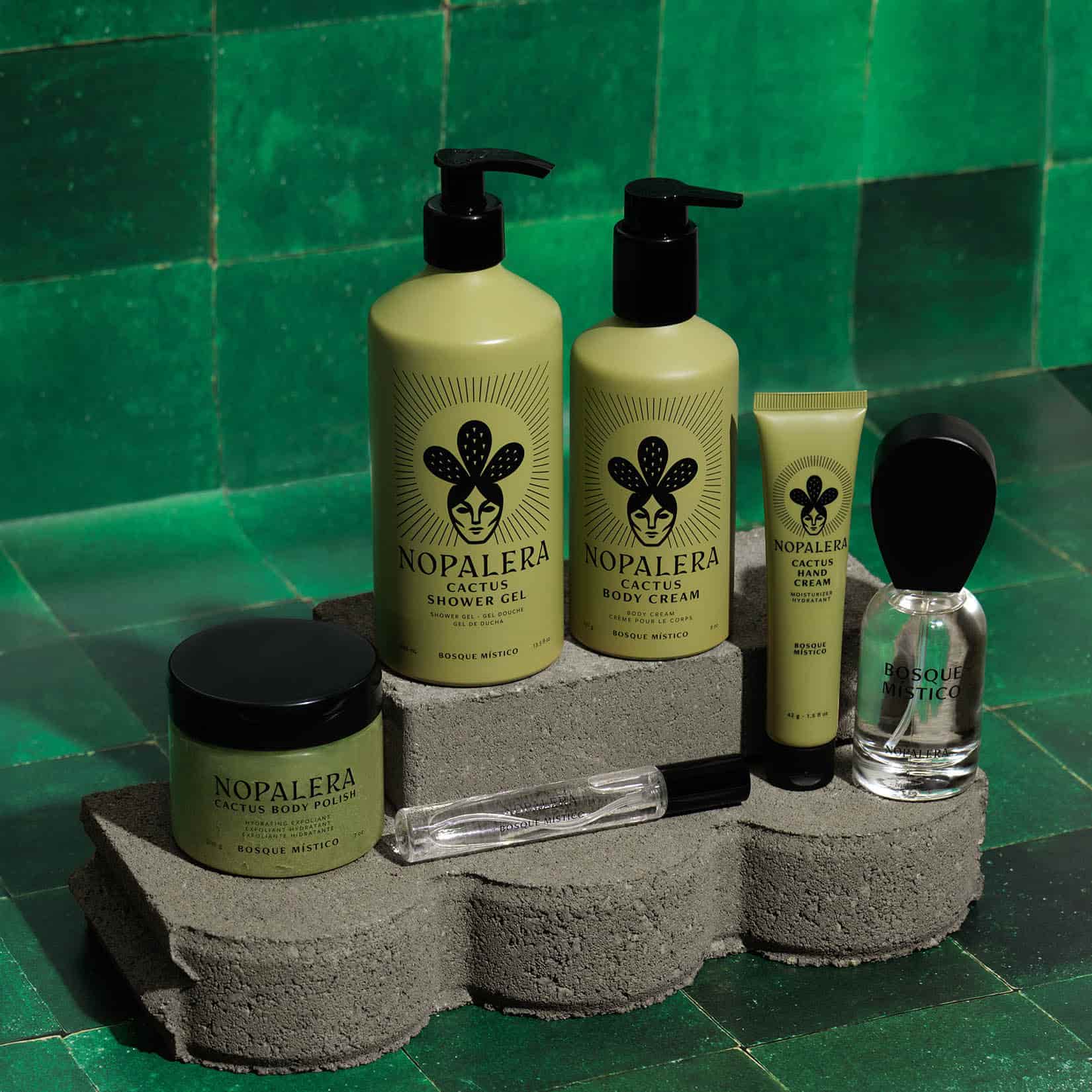 Nopalera body care and fragrance Bosque Místico collection featuring shower gel, body cream, body polish, hand cream,  perfume 50 ml and travel spray displayed on stone blocks against green tile.