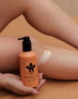Person holding a bottle of Nopalea Cactus Body Cream Flor de Madera on a tan surface