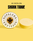 A white lotion bar displayed in front of a tin with the Nopalera brand logo. The background is yellow with the text 'AS SEEN ON SHARK TANK' at the top.