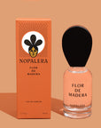 A glass of a 50ml Luxury Mexican fragrance  bottle of Flor de Madera perfume with a wooden cap, alongside its orange packaging box with the brand name Nopalera and product title.