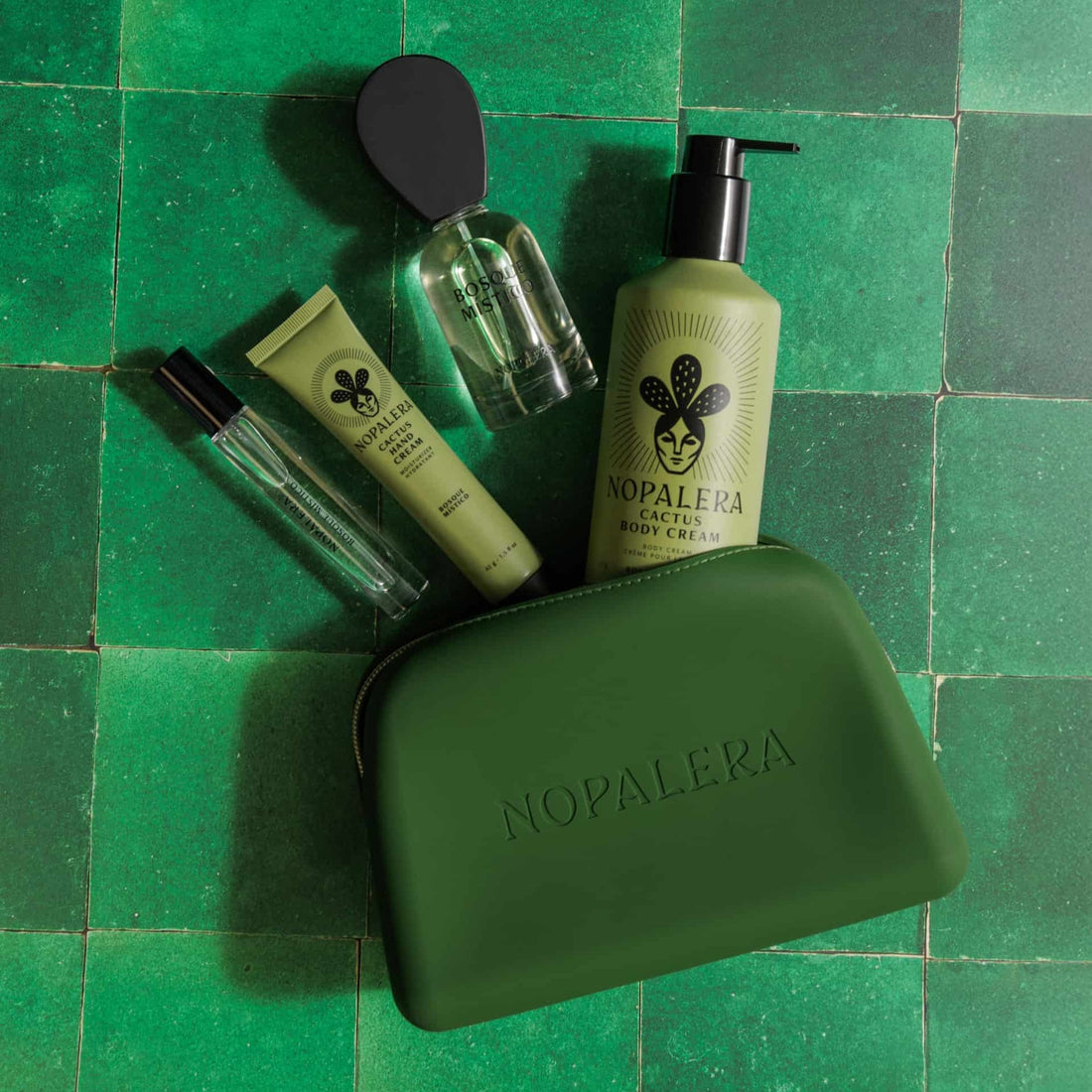 Nopalera skincare products on a green tiled background and a Green Nopalera cosmetic pouch with gold zipper and embossed logo 
