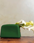 Green Nopalera cosmetic pouch with gold zipper and embossed logo on a neutral background and flowers