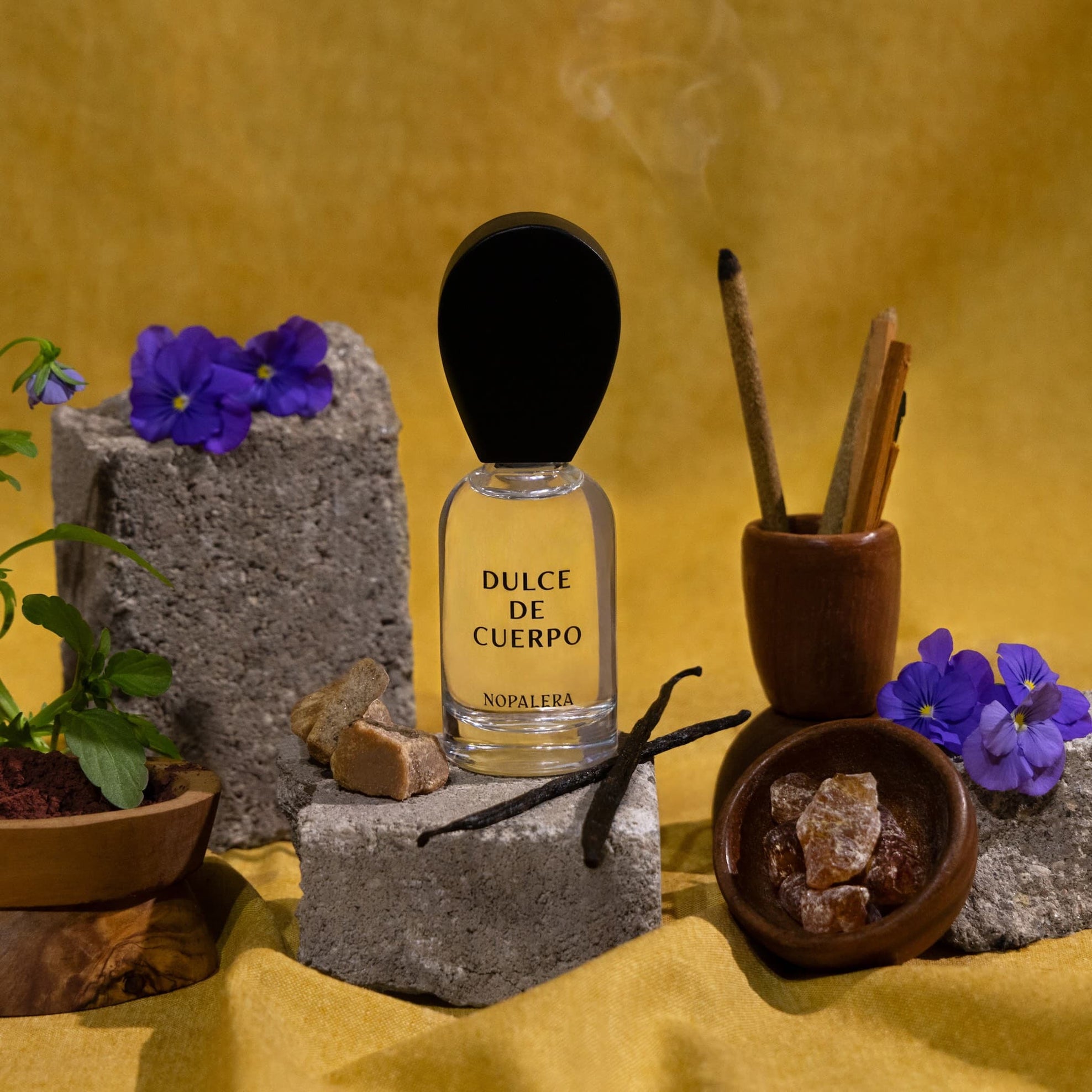 Nopalera Perfume bottle labeled 'Dulce de Cuerpo' with incense sticks, flowers, and vanilla beans on a yellow background.