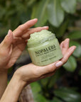 Person holding a jar of Nopalera Cactus Body Polish against a green leafy background