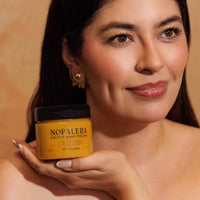 Woman holding a jar of Nopalera Cactus Body Polish  tangerine against an orange background
