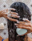 Hands holding Nopalera Moisturize and Shine shampoo bar in the shower