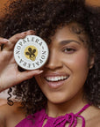Model holding Nopalera citrus lotion bar tin with curly hair and natural glow.