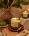 lit Nopalera Mérida scented candle in green glass jar on wooden bath tray