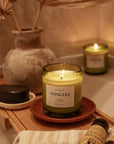 lit Nopalera scented Tepoztlan candle in green glass jar on wooden tray in bathroom