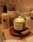 Nopalera Todos Santos scented candle lit in green glass jar on wooden bath tray